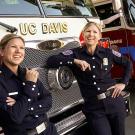 Two identical twins standing in front of a fire truck.