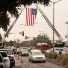 Firetrucks hoist American flag over road.