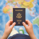 A person holds U.S. passport against backdrop of world map.