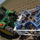 Large tractor pulls frame-like equipment with cameras through tomato field.