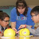 Photo: two young students and a woman examine two grapefruits set up to conduct energy