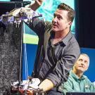 Man demonstrating Mars rover on strings lowering to ground, as another man in background looks on