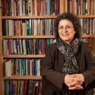 Suad Joseph, sitting at table, hands folded, in front of bookcases.