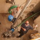 Photo shot from above showing three men in a room with a hose connection