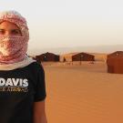 Woman wearing headscarf and UC Davis Quarter Abroad shirt while standing in a desert