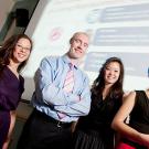 Four people, a woman, a man and two women posing in front of a PowerPoint screen in the background