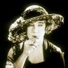 Screenshot from a 1924 film of a woman in a feathered hat smoking a cigarette