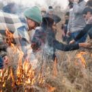 Men and women in jackets light field of deergrass on fire as part of cultural burn in California.