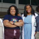 A group of four women stand together in front of a medical office building. Two wear lab coats and one wears scrubs. One has a stethoscope. All are smiling and looking directly at us.