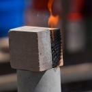 An earth block sits next to a block of wood, with a flame of fire coming from the charred wood after being blowtorched. 