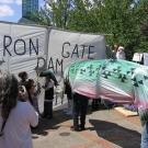 Klamath Basin tribes protest in 2006 with banner representing Iron Gate dam and large salmon costume appearing to be blocked behind it