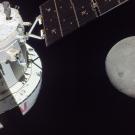 Photo taken in space with part of a spacecraft on the left and the moon on the right. 