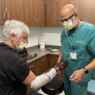 Dave Brockman, a hand amputee, wears a myoelectric prosthesis that looks like a red and black glove. He sits in front of his orthotist who is making sure the fit is correct.