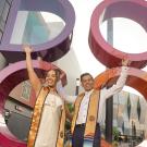 Two UC Davis students in graduation stoles in front of the colorful DOCO sculpture in downtown Sacramento.
