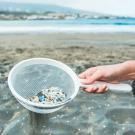 Hand of young woman uses sieve to collect microplastic at ocean beach
