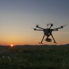 drone flies over open field at sunset