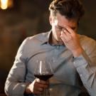 Man rubbing his forehead while drinking red wine. UC Davis scientists theorize that a flavanol found naturally in red wine can interfere with the metabolism of alcohol and cause "red wine headache."
