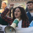 People in crowd holding signs, shouting into megaphone