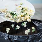 person's hand scraping plate of pasta and vegetables into trash can
