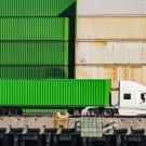 bright green heavy-duty truck sits parallel to stack of cargo containers at shipping port