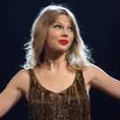 Singer Taylor Swift in sequined top holds arms out with black background