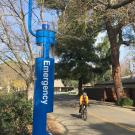 Blue-light emergency call station along Sprocket Bikeway, with bicyclists passing by