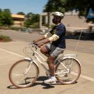 Chancellor Gary S. May, in shorts and mask, riding bicycle with "UC Davis Chancellor" pennant.