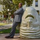 Chancellor Gary S. May, leeaning on "Eye on Mrak" Egghead sculpture