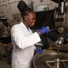 Woman in lab coat works with large coffee roaster
