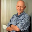 Man with short-sleeved blue shirt poses for photo near wall