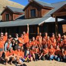 People wearing orange shirts pose in front of cabin.