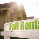A white sign with "Fall Rental" in green lettering against part of an apartment building 