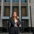 A student poses in front of a court building wearing a suit. 