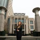 A political science major in a suit stands in front of a courthouse with her arms crossed
