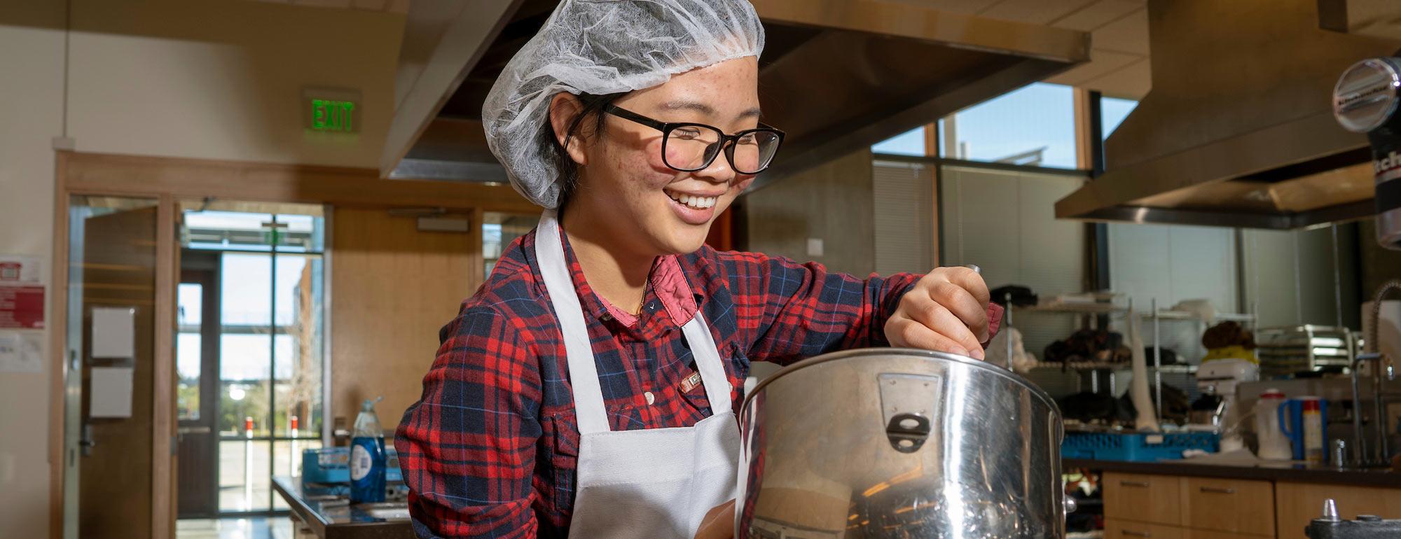 A female student mixes a food preparation in the UC Davis food lab
