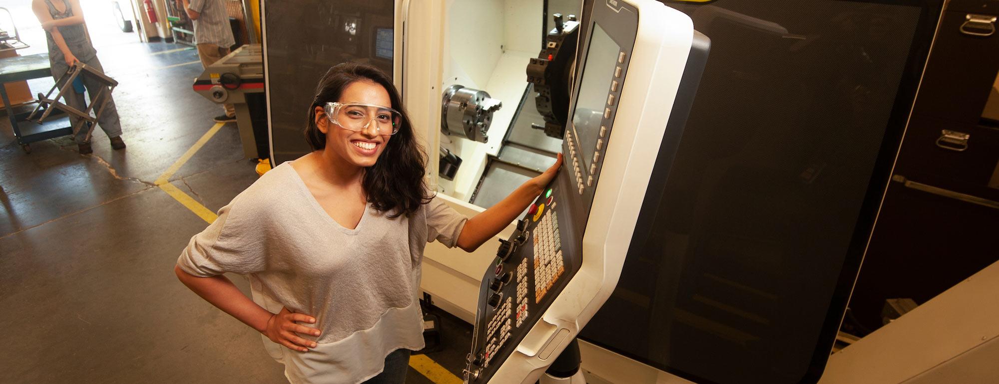 A female student in safety glasses exhibiting some machinery