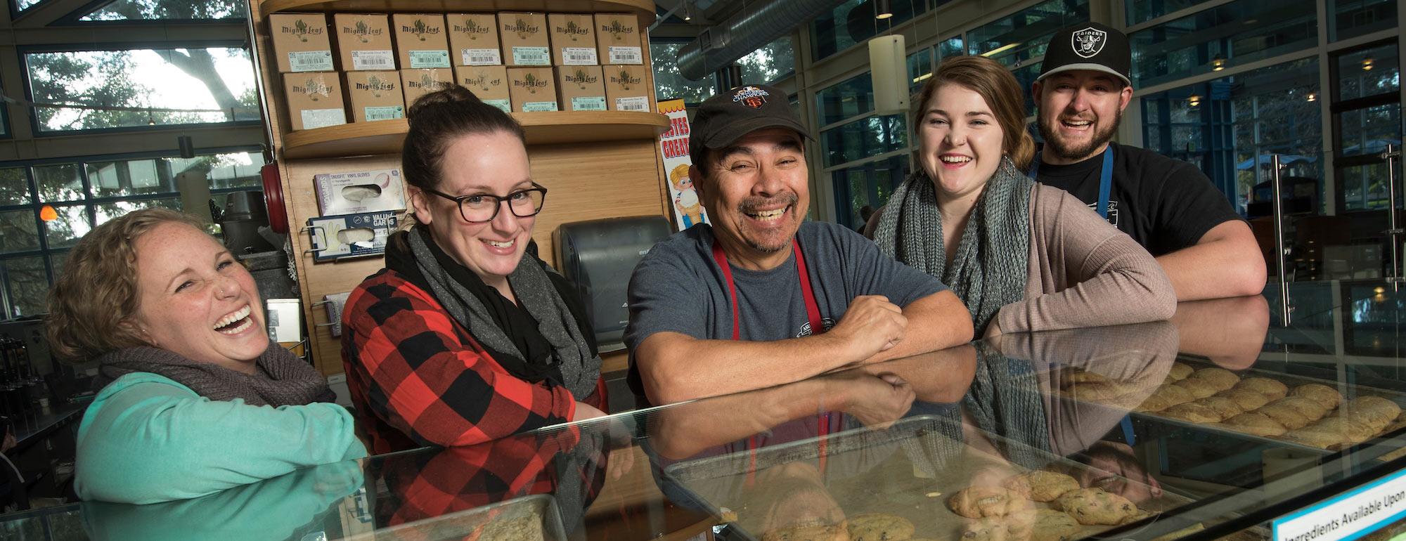 Student Coffee House workers smile with their manager over a counter filled with baked goods