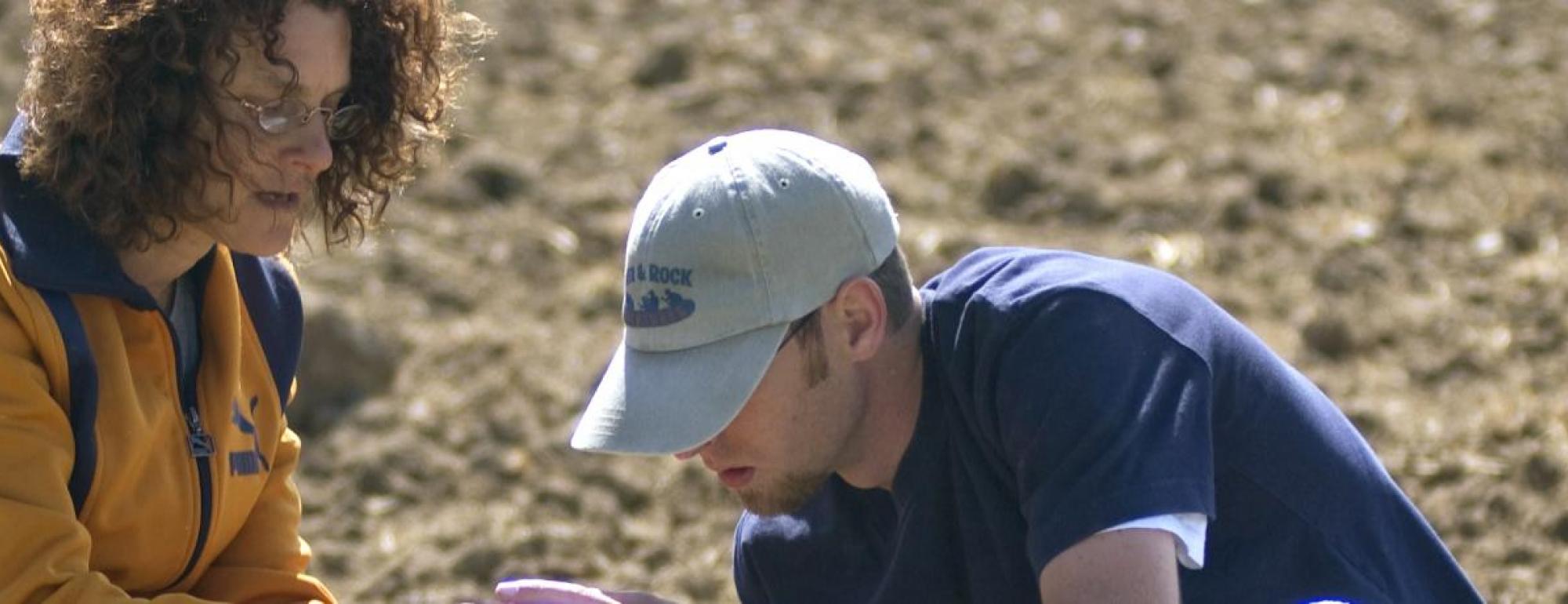 two uc davis students lean over working in dirt field