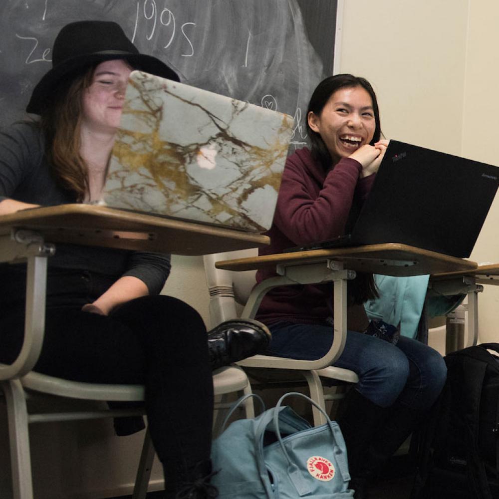 Students sit at desks smiling behind their laptops