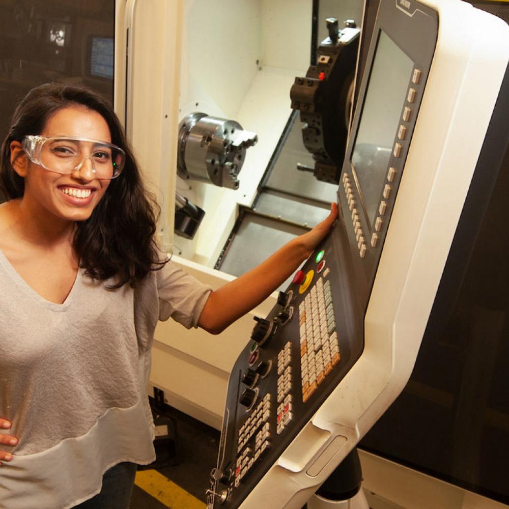 A female student in safety glasses exhibiting some machinery