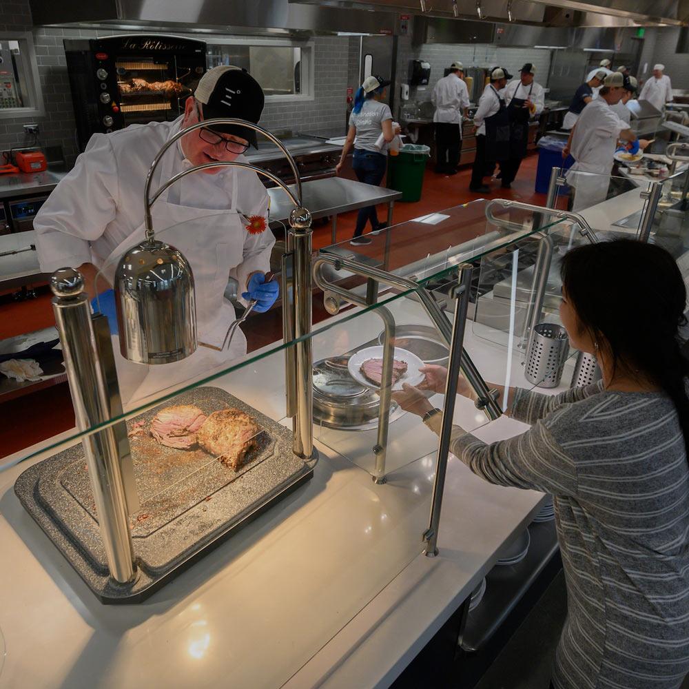 A dining commons employee serves a cut of meat to a UC Davis student