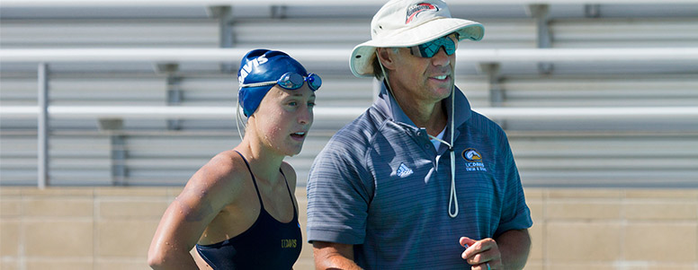 Swim coach Pete Motekaitis talks with a female swimmer at a pool