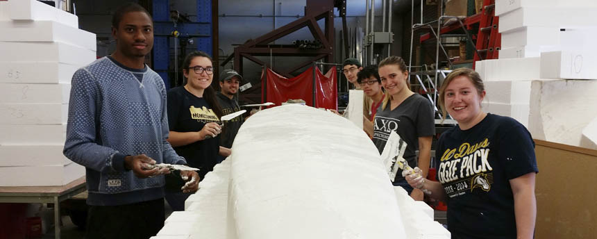 A group of students apply concrete to a canoe mold