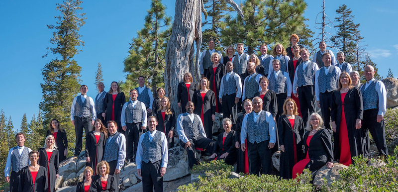 The Sacramento Master Singers standing outdoors on a hill in front of a tree.