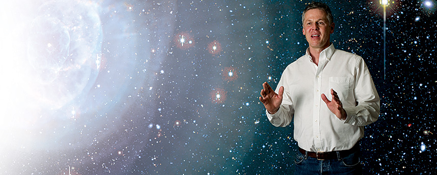 Photo illustration with a man standing and talking in front of a photo of the cosmos