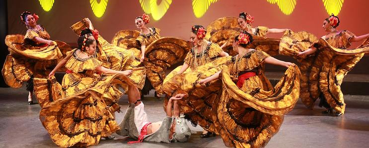 Several women in ornately and colorful dresses dancing on stage.