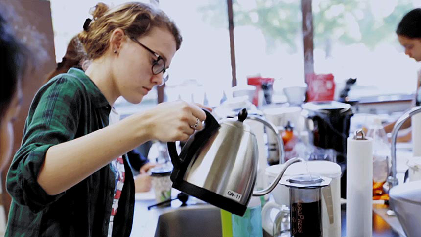 Woman in lab pours coffee from metal pot