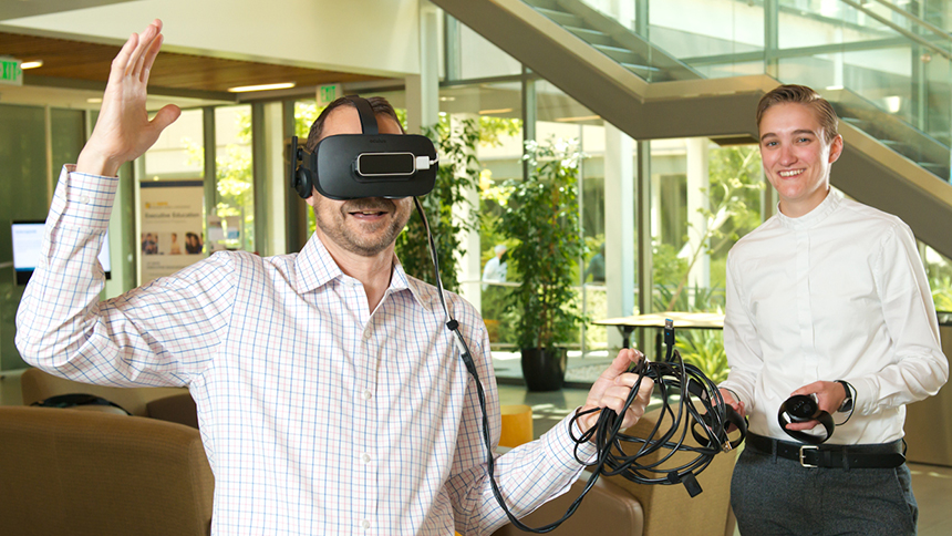 A man wears a virtual-reality headset while a woman looks on