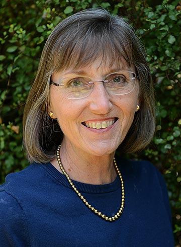 Woman with glasses wearing royal blue top and gold beads