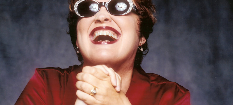 Diane Schuur smiling, wearing sunglasses, with lights relfected in the sunglasses' lenses.